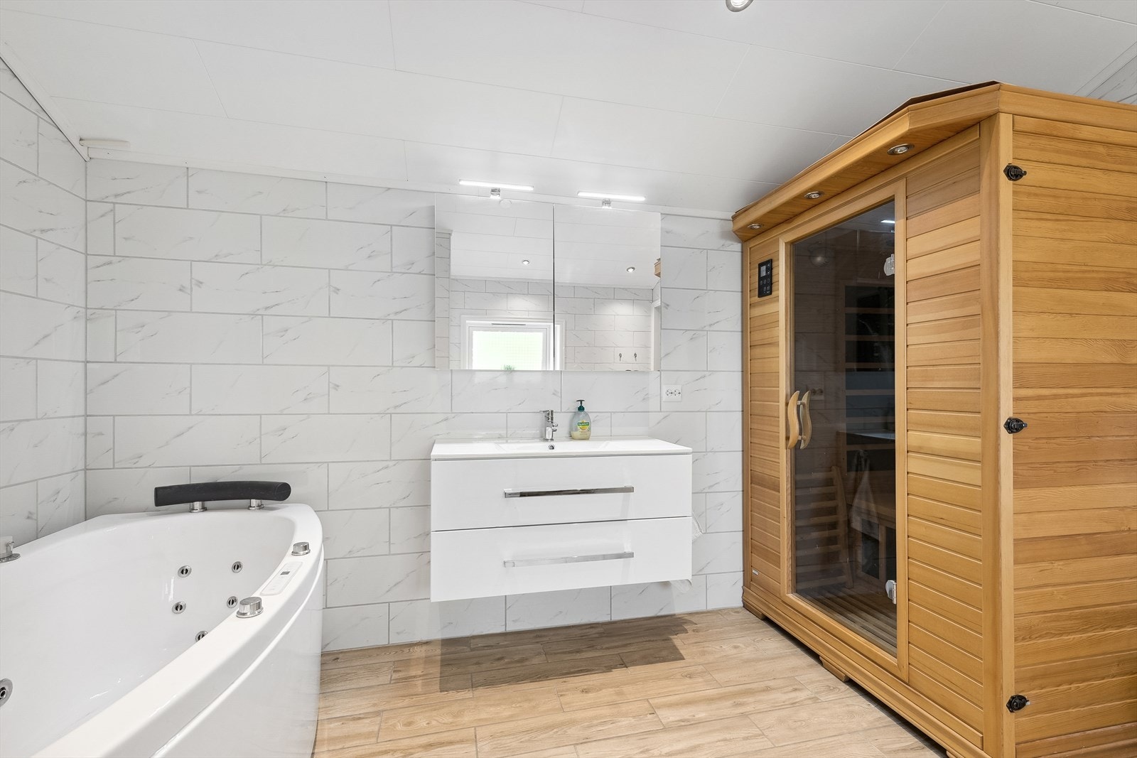 Badet er innredet med veggmontert klosett, dusjkabinett, saunakabin, opplegg til vaskemaskin og badekar. Galleribilde