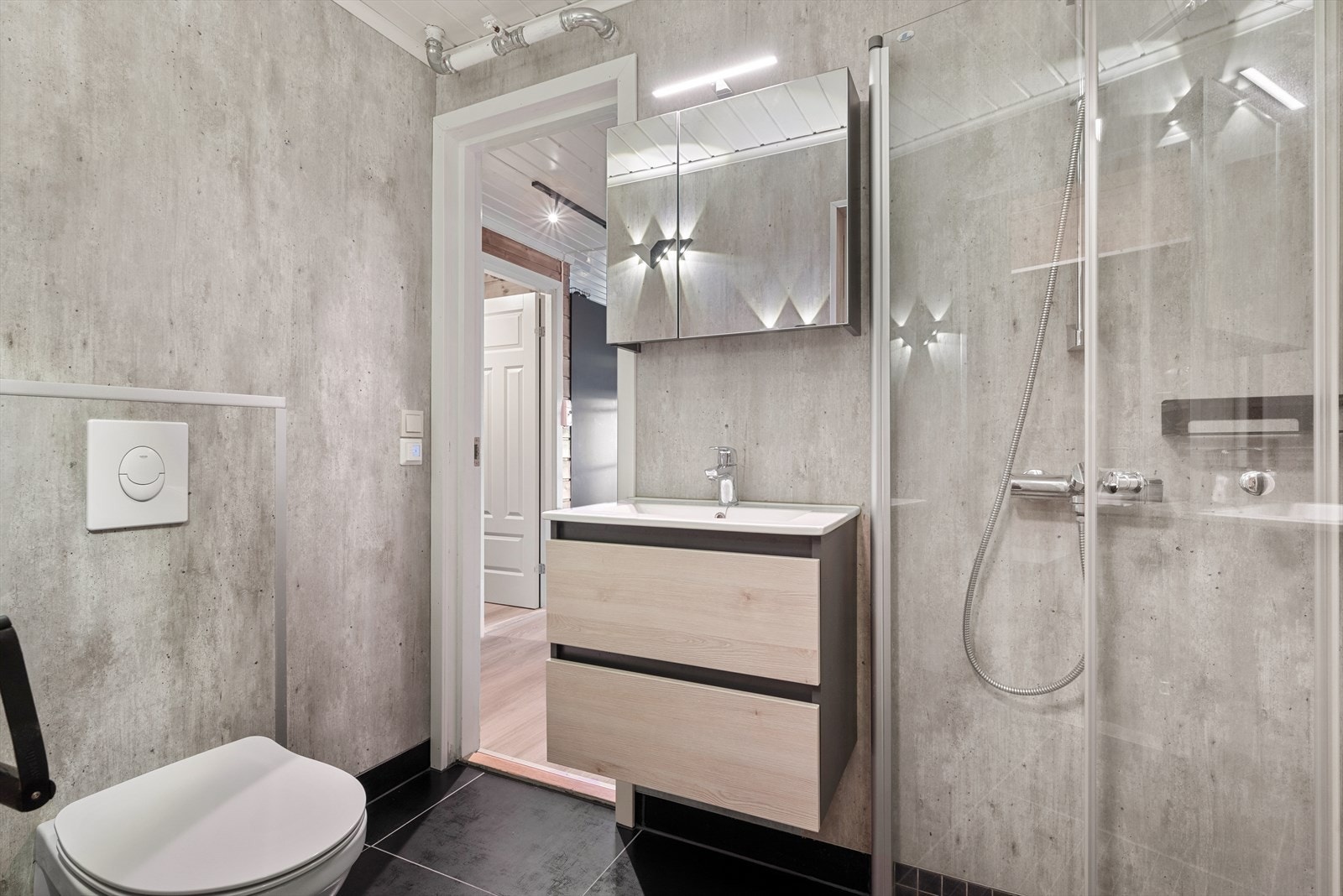 Badet har grå våtromsplater i betongimitasjon på veggene og sorte fliser på gulv med gulvvarme. Galleribilde