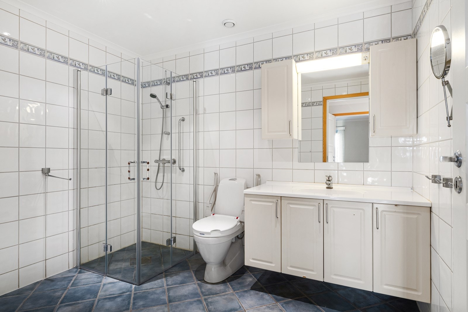 Badet har servant i baderomsinnredning, dusj på vegg med glassdører, og toalett. Et innbydende rom som legger til rette for både avslapning og hverdagsluksus. Galleribilde