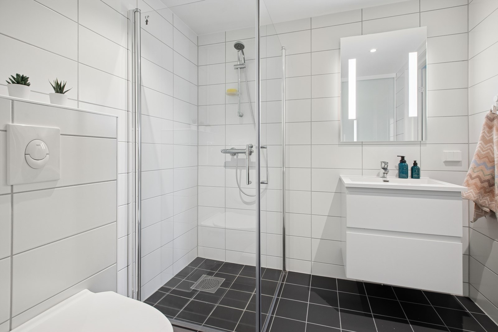 Badet er pent flislagt med varmekabler i gulv. Rommet er innredet vegghengt toalett, servantinnredning med speil- og lys og dusjhjørne med glassdører. Galleribilde