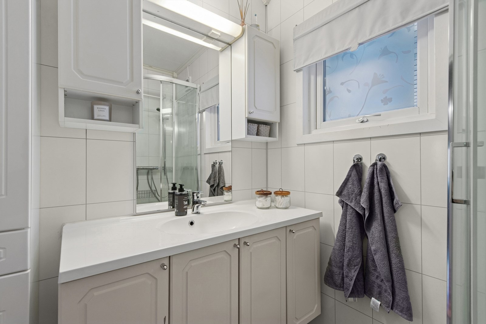 Baderom med våtromsplater på veggene og innredning med servant og skap. Galleribilde