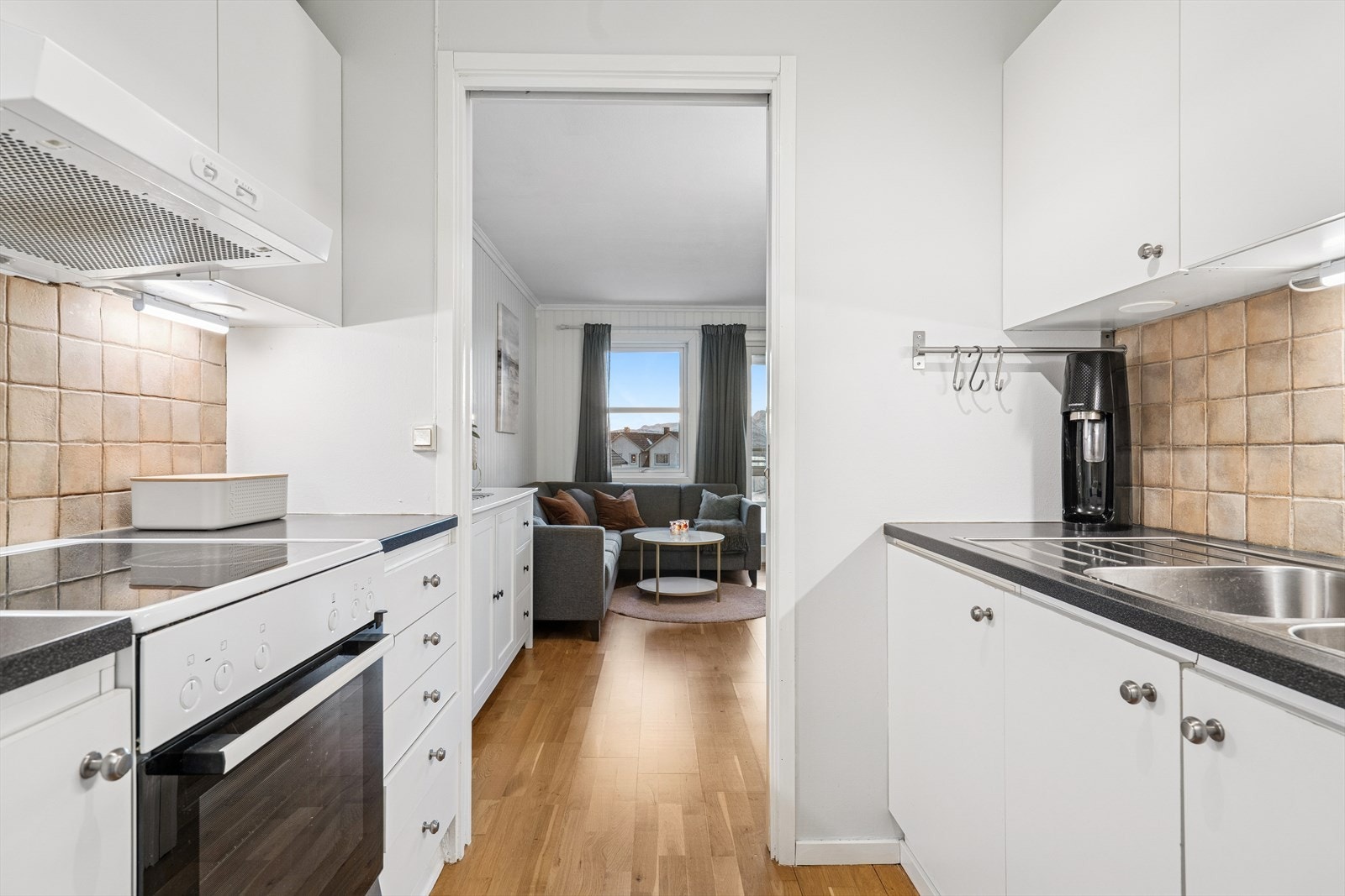 Kjøkkenet har en tidløs innredning med lyste glatte fronter, laminert benkeplate med nedfelt stålvask og fliser på vegg over benk Galleribilde