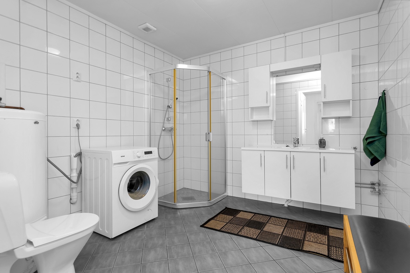Bad med toalett, dusjhjørne, servant og opplegg for vaskemaskin. Galleribilde