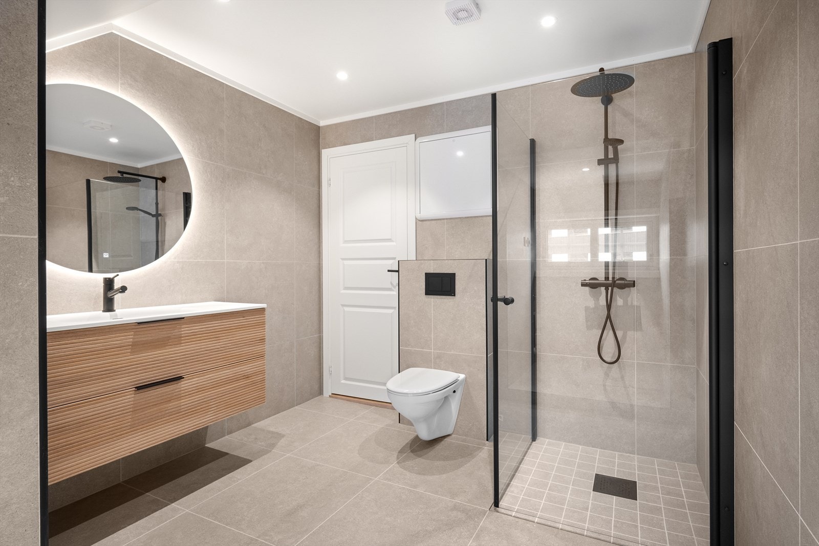 Romslig, flislagt bad med fine fargevalg. Utstyrt med vegghengt toalett, dusj med innfellbare dører og innredning med servant. Galleribilde