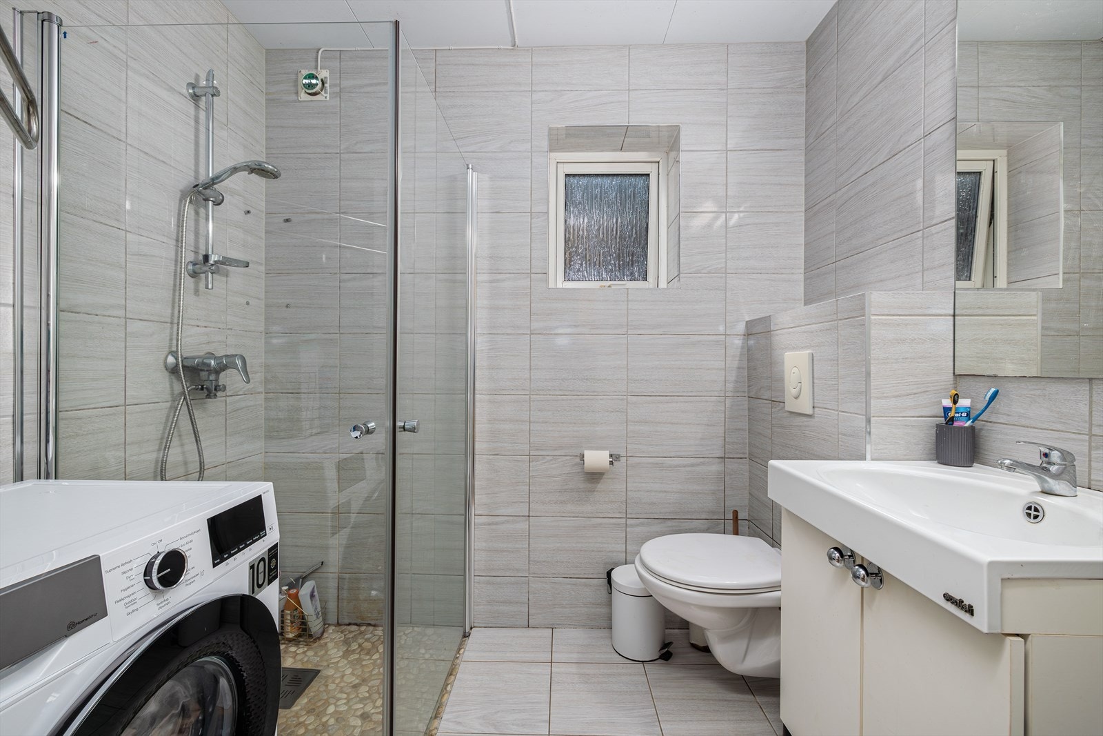 Bad/vaskerom: nedfelt servant, vegghengt klosett, dusjhjørne, speil og opplegg til vaskemaskin. Gulvvarme Galleribilde