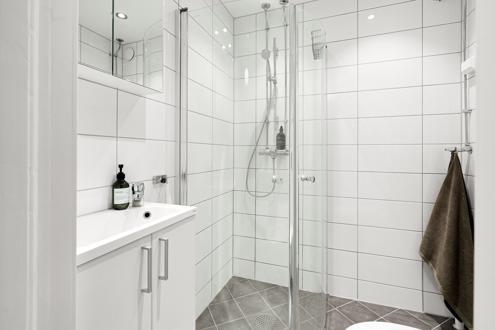 Bad med dusjhjørne, vegghengt toalett og servant med tilhørende speilskap. Galleribilde