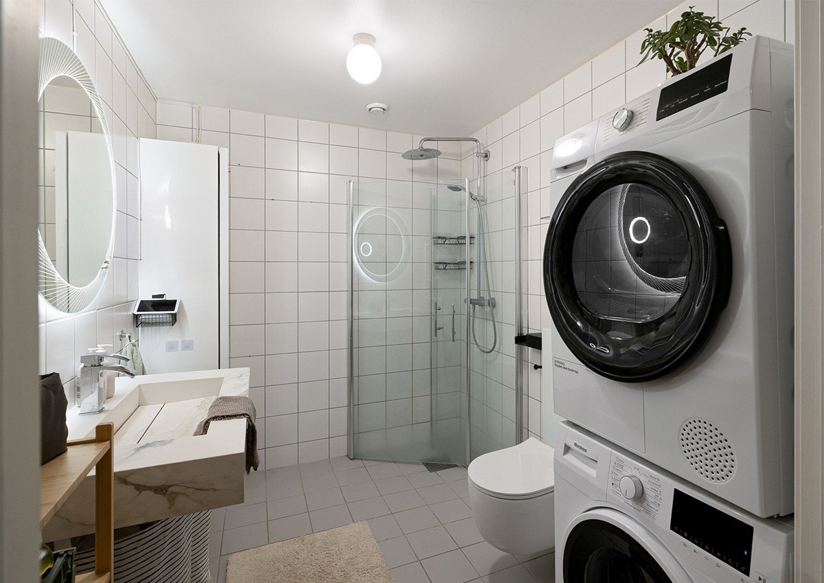 Lyst og pent baderom med flislage overflater, gulvvarme og opplegg for vaskemaskin og tørketrommel. Galleribilde