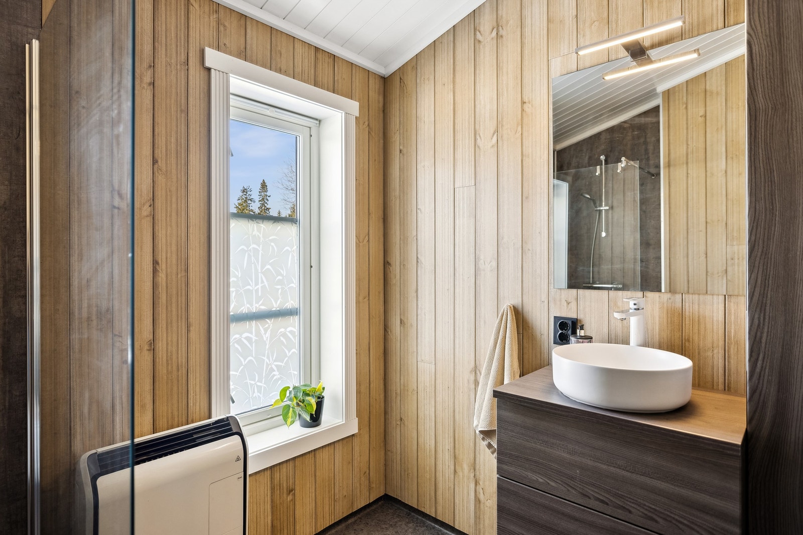 Pent bad med vinylbelegg på gulv og baderomsplater samt panel på vegger. Dansani baderomsinnredning med servant, speil med lys og dusjnisje med glassvegg. Galleribilde