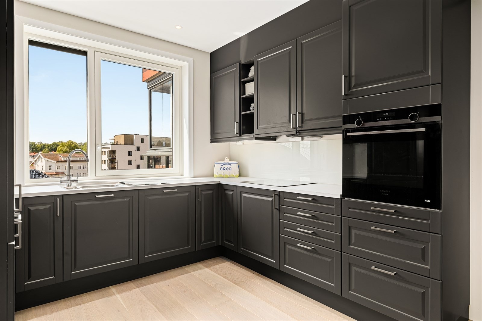 Kjøkkenet er lyst, åpent og svært innbydende - et perfekt sted for både hverdagsmat og større sammenkomster. De profilerte frontene gir et tidløst og klassisk uttrykk, mens den laminerte benkeplaten kombinerer slitestyrke med et stilrent utseende. Galleribilde