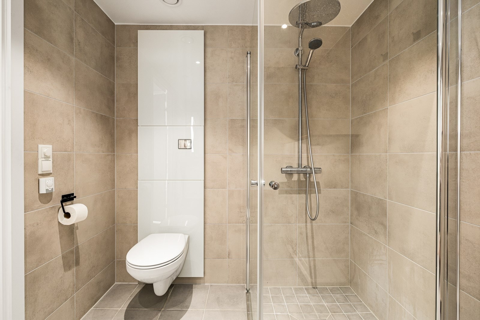 Baderommet fremstår stilrent og gjennomført, med flislagte vegger og gulv. Den malte himlingen er utstyrt med innfelte downlights som gir behagelig og funksjonell belysning. Vannbåren gulvvarme sørger for lun komfort. Galleribilde