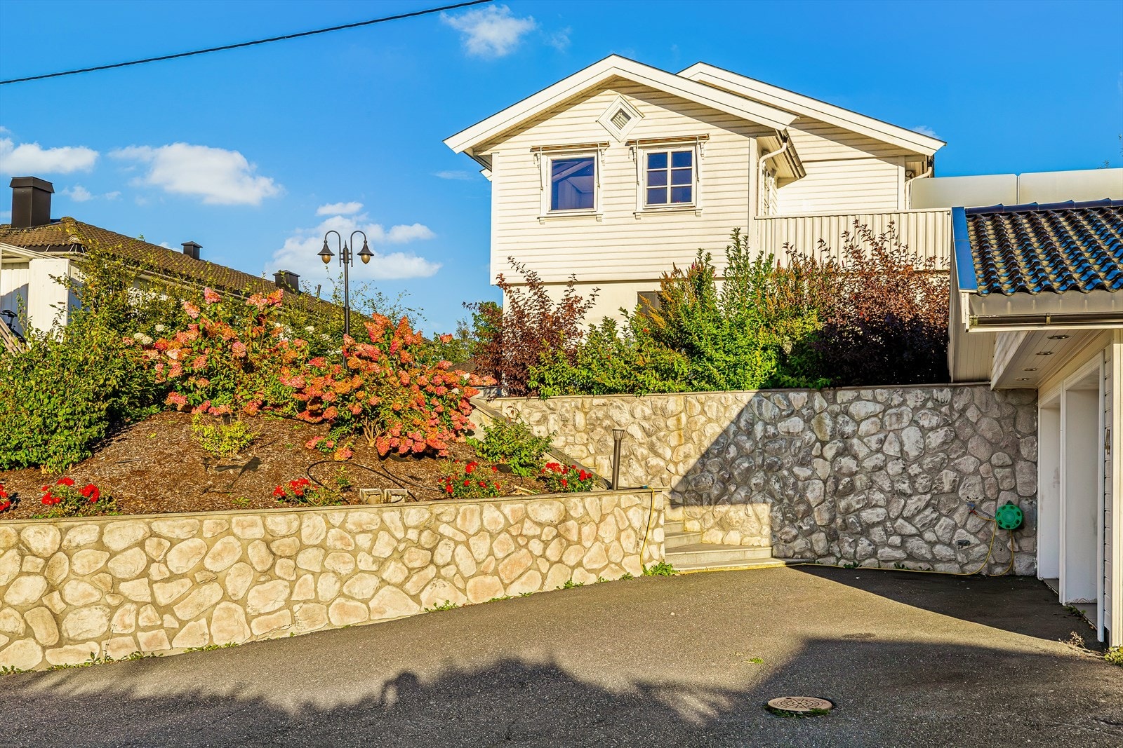 Asfaltert og romslig gårdsplass kombinert med pent opparbeidede blomsterbed - gir et flott førsteinntrykk og en praktisk, vedlikeholdsvennlig uteplass. Galleribilde