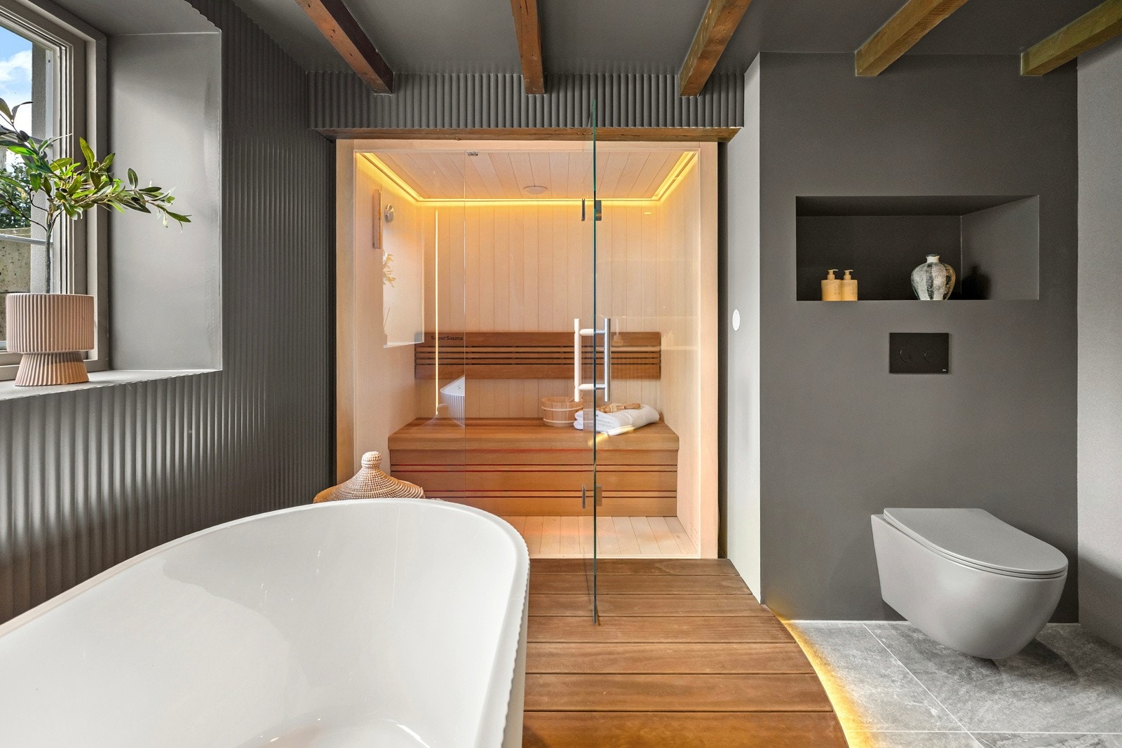 Et frittstående badekar, med gulvmontert kran, er plassert på skipsgulvet, og det er glassvegg og glassdør inn til en deilig badstue. Galleribilde