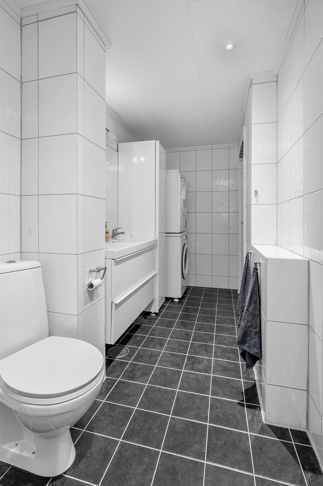 Baderom med fliser på gulv og vegger - dobbel servant, toalett, opplegg for vaskemaskin og dusj Galleribilde