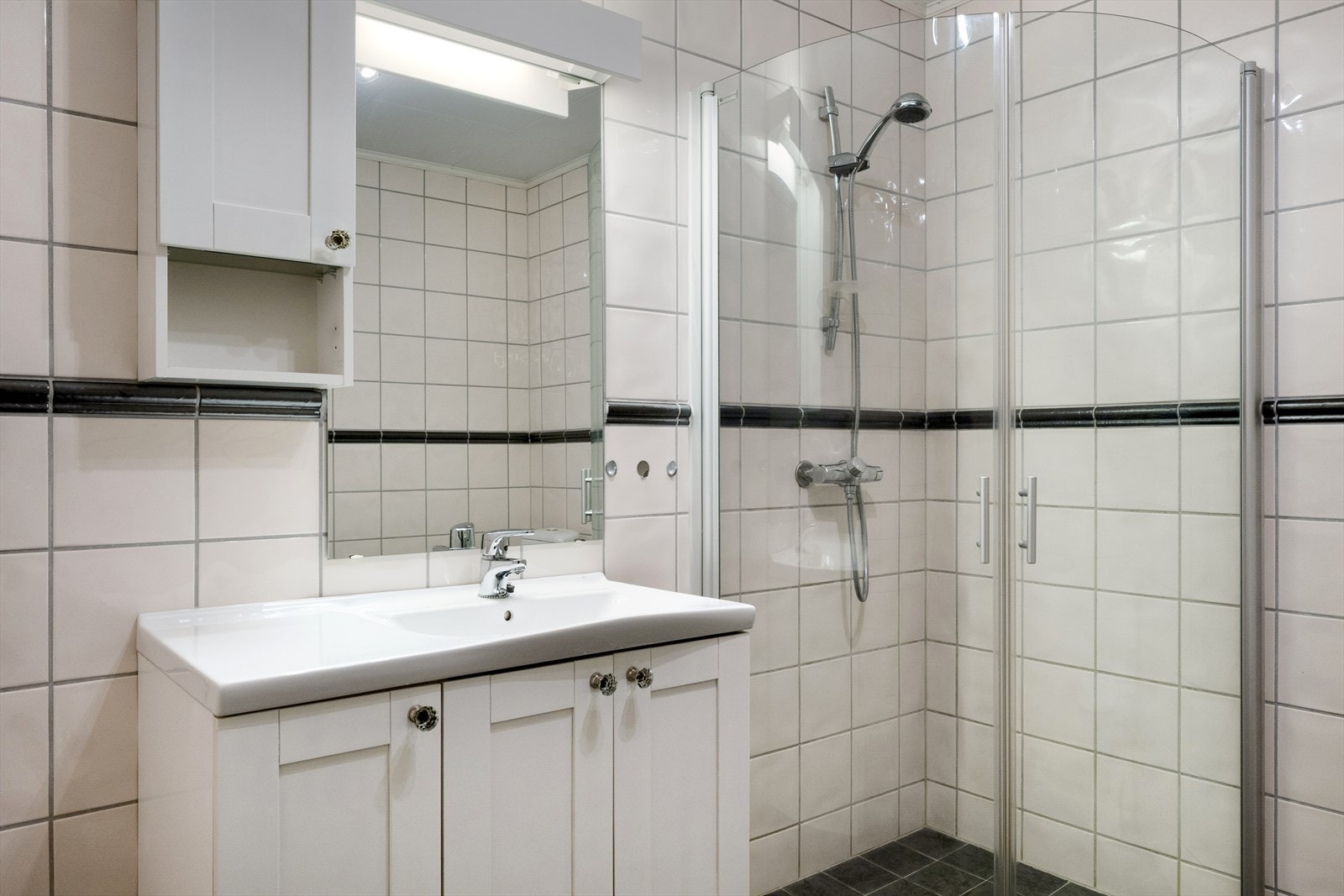 Den klassiske, lyse innredningen har heldekkende servant og tilhørende overskap. De buede dusjveggene kan felles inn, og det er gulvmontert wc. Galleribilde