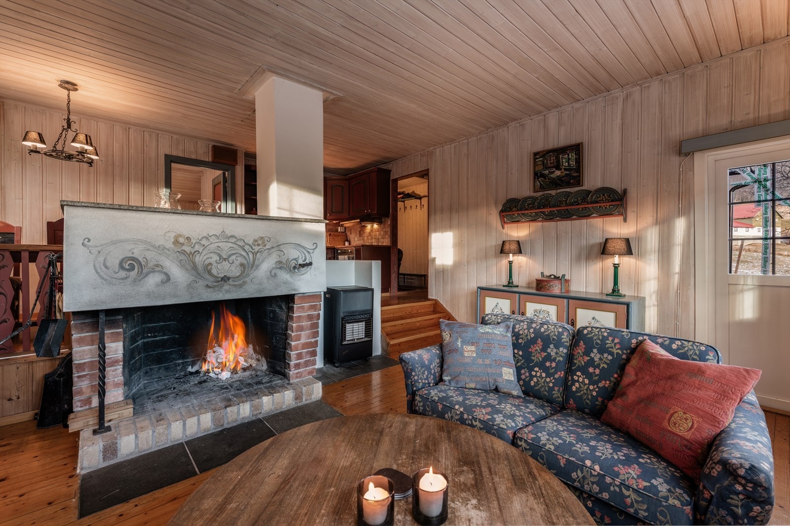 Hyggelig stue med åpen løsning mot kjøkken og spisebord. Peis med åpen grue. Galleribilde