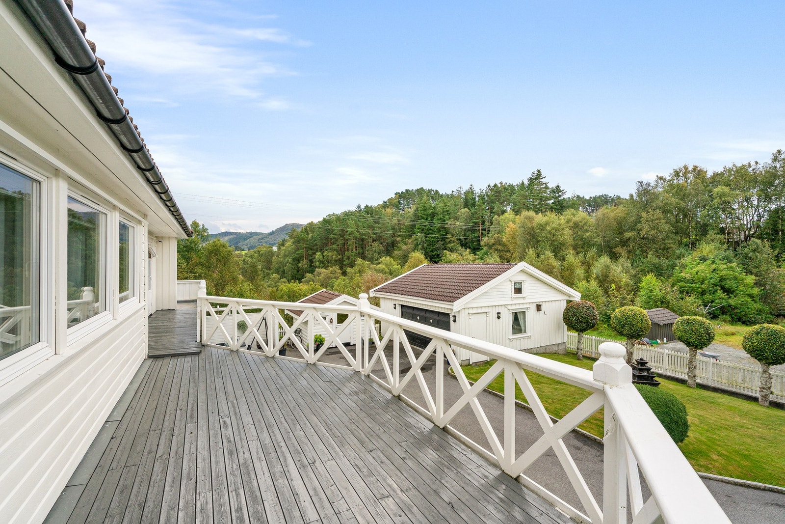 Langstrakt balkong med utsikt mot grønne omgivelser og tunet foran eiendommen. Galleribilde