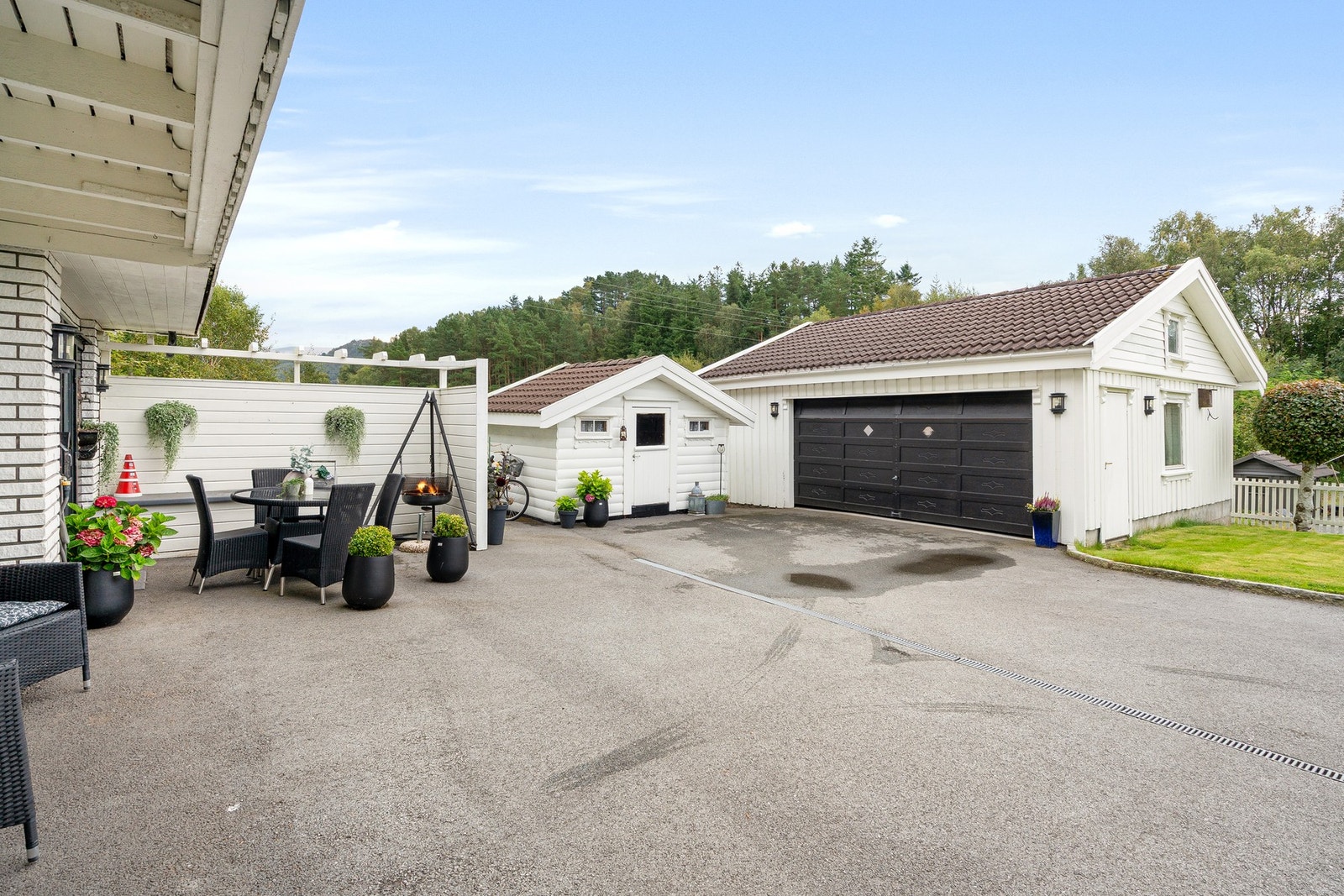 Romslig gårdsplass med dobbelgarasje, bod og en skjermet sittegruppe ved husveggen. Galleribilde