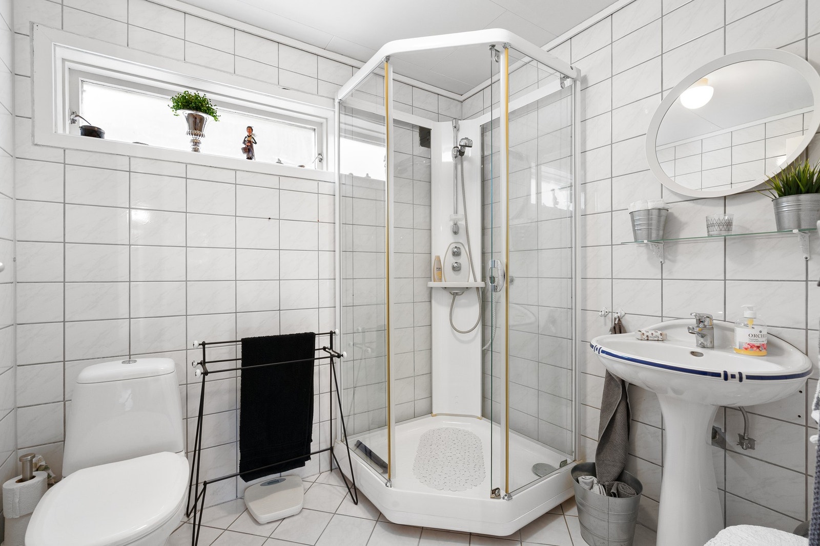 Lyst baderom med dusjkabinett, praktiske løsninger og et vindu som gir luftig preg med lys gjennom vinduene. Galleribilde