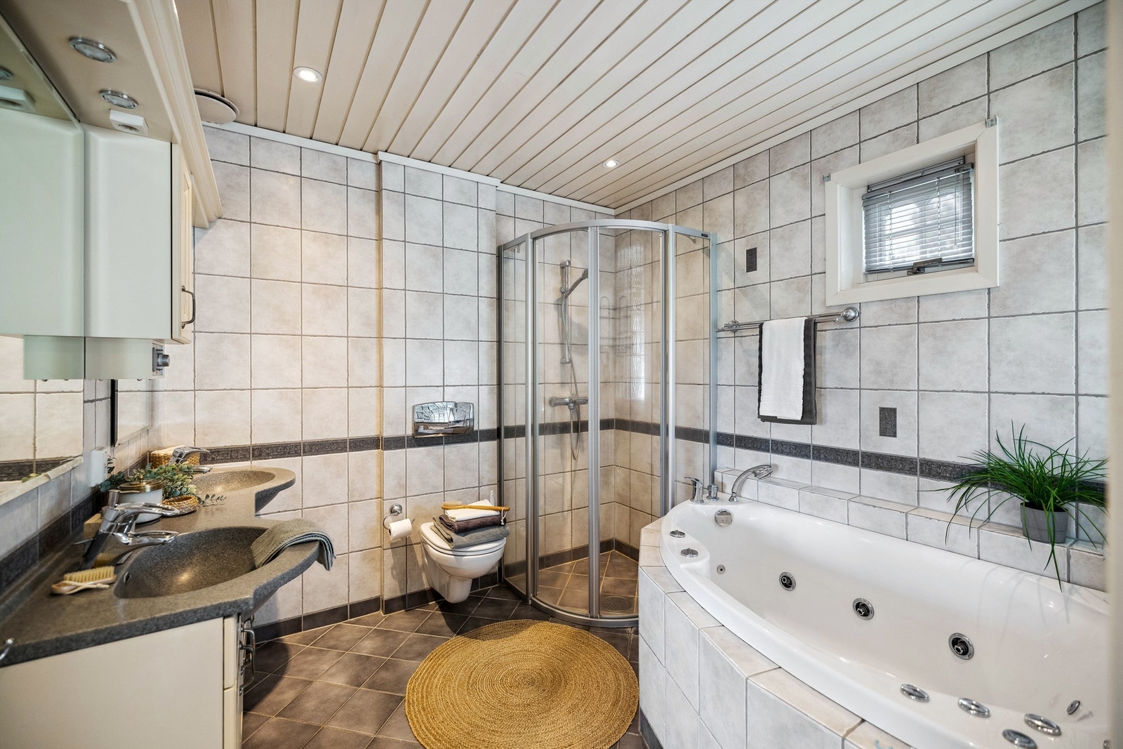 Bad med vegghengt WC, dusjhjørne og innfliset boblebad. Dobbel vask nedfelt i innredningen Galleribilde