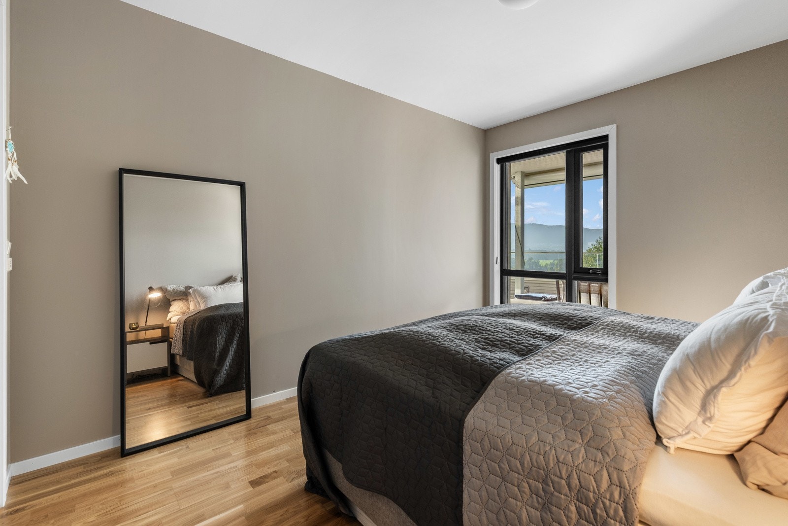 Et rom som inviterer til avslapning, med store vinduer, lune fargetoner og god plass til både seng og garderobeløsning. Galleribilde