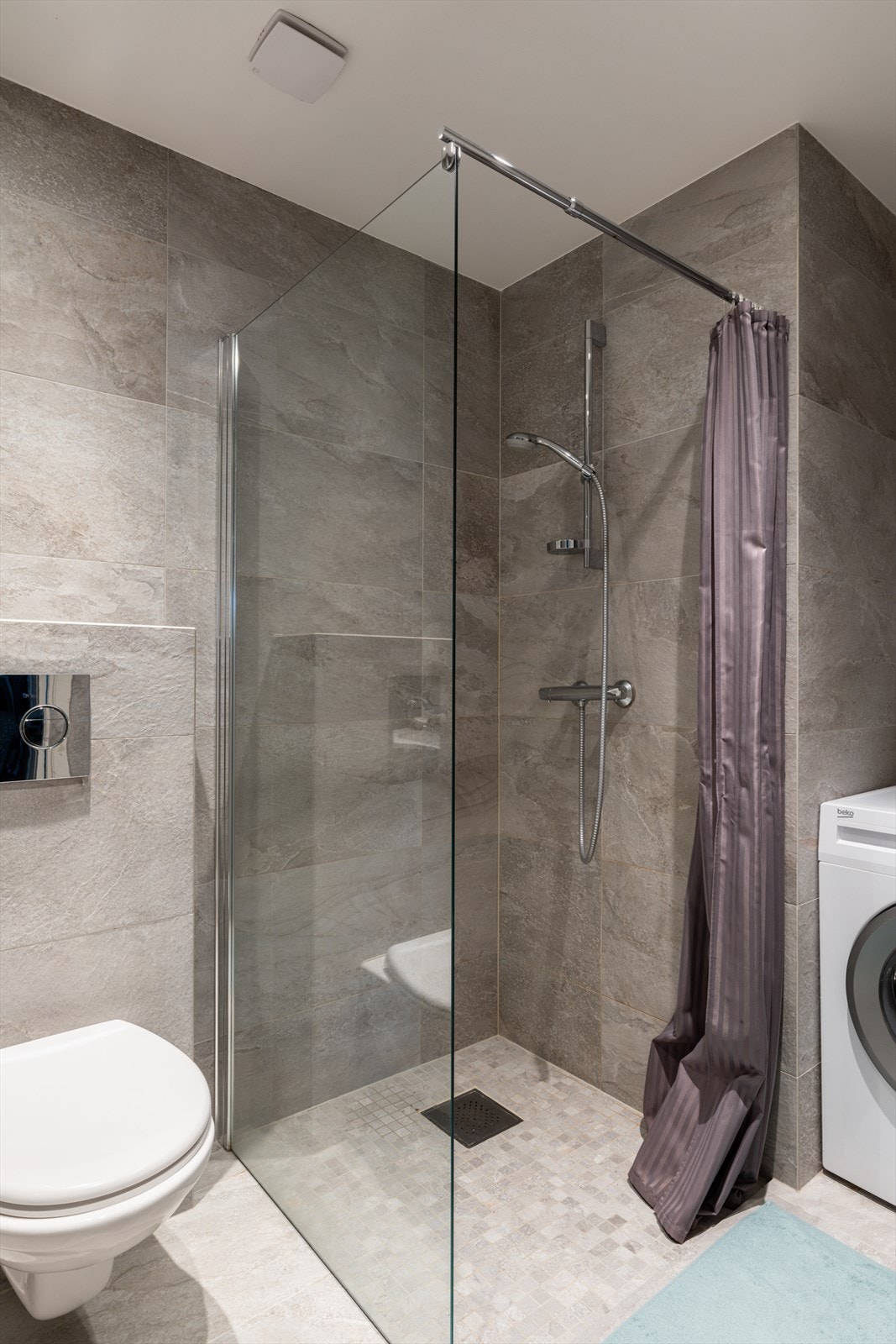 Badet er helfliset og utstyrt med servantskap, speil, vegghengt toalett, dusjsone med glassdører og opplegg for vaskemaskin. Galleribilde