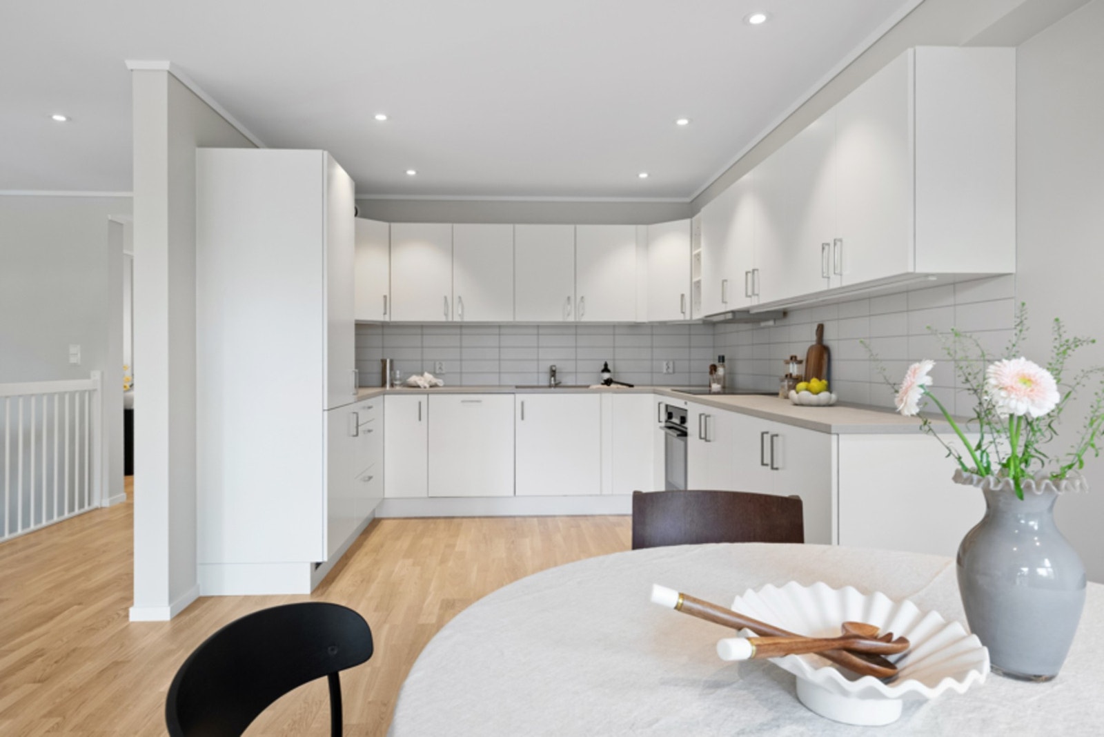 Innredningen har hvite, glatte fronter, lysgrå benkeplate med planlimt vaskekum og hvite flisplater over benken. Galleribilde