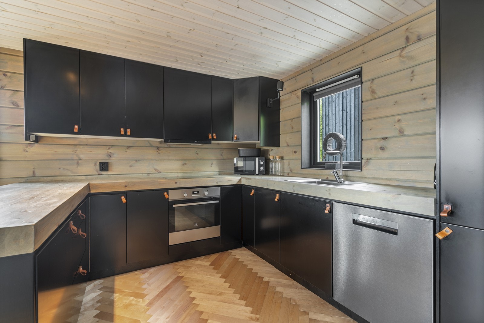 Lekkert kjøkken med flott benkeplate i massiv heltre. Stilige detaljer som skinnhåndtak, kombinert med gjennomgående innslag av sort og krom, gir kjøkkenet et moderne og eksklusivt preg Galleribilde