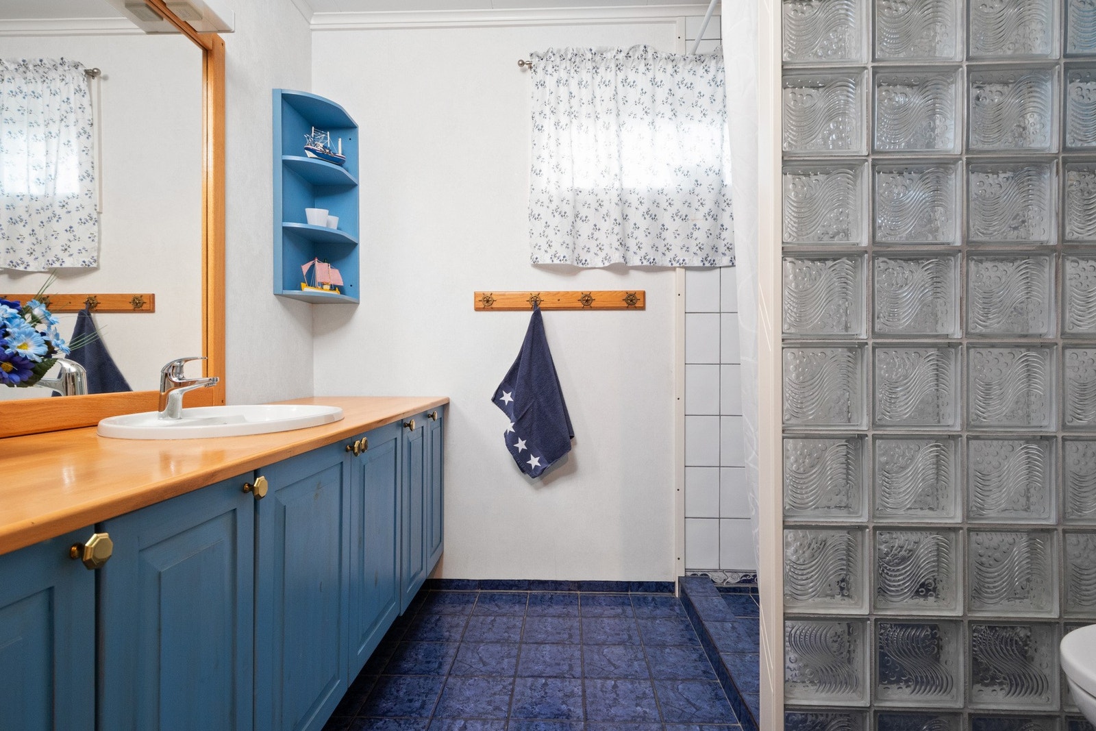 Badet i underetasjen har hvitmalte vegger, hvite fliser i dusjsonen og blå fliser på gulv med gulvvarme. Galleribilde