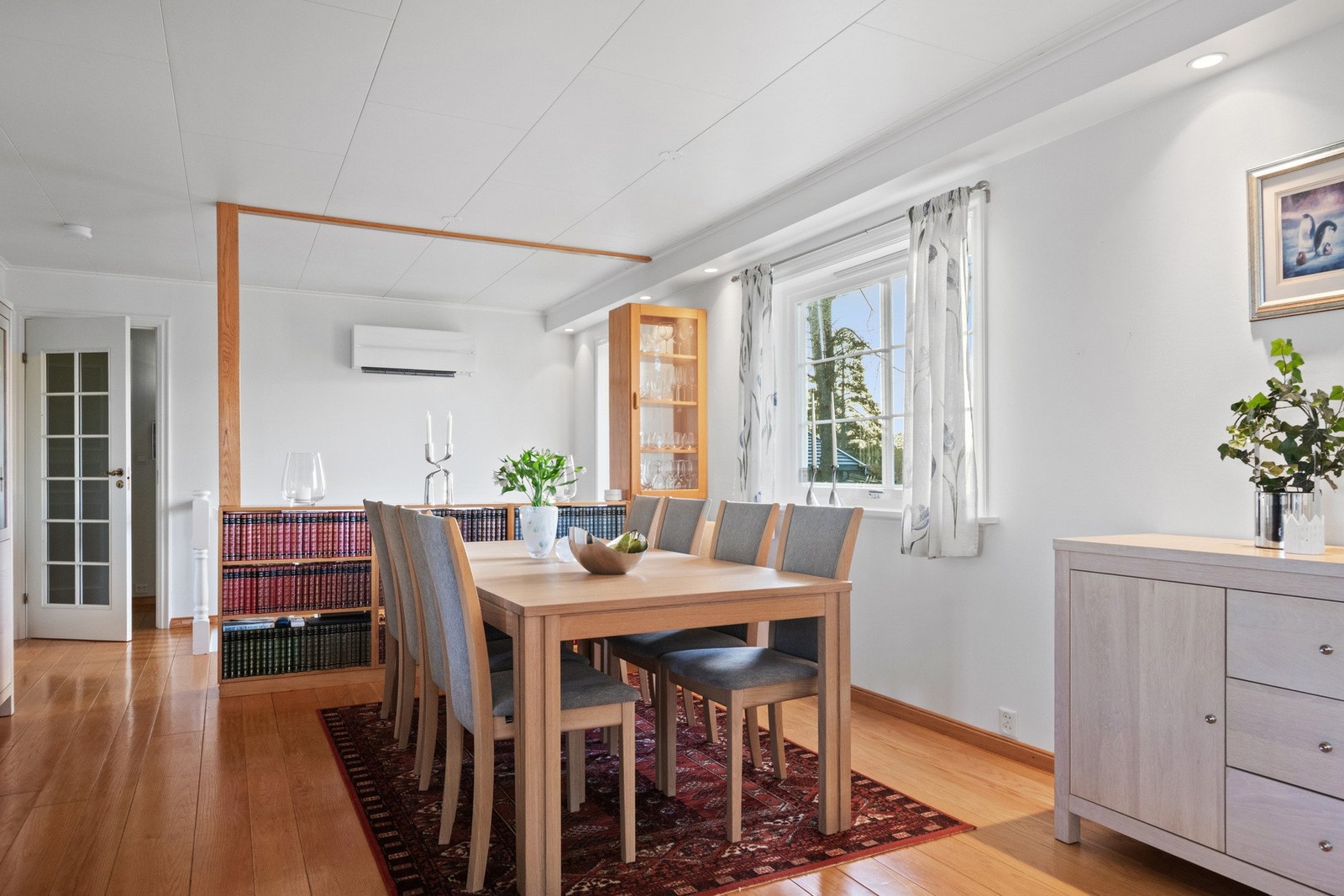 Stuen har grå- og hvitmalte vegger mot gyllent heltregulv, og dagslyset strømmer inn via store vinduer i tre himmelretninger. Galleribilde