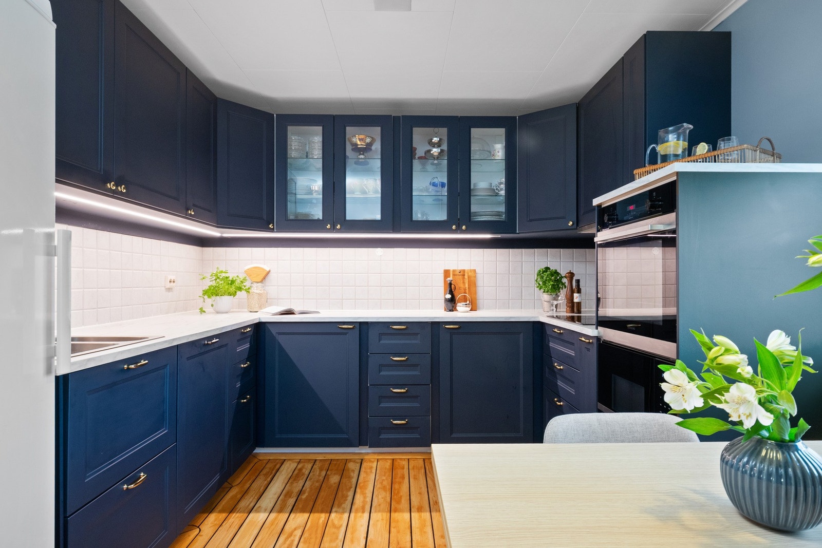 Innredningen har mørkeblå, profilerte fronter, vitrinedører og hvit laminatbenkeplate med nedfelt kum i stål. Galleribilde