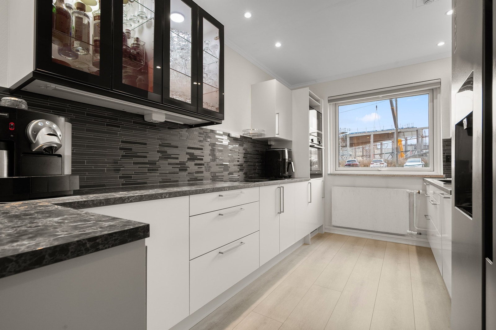 Kjøkkenet er utstyrt med integrerte hvitevarer og induksjonstopp med ventilator, stekeovn og oppvaskmaskin. Overskap fra Ikea med svarte glassfronter ble supplert i 2023 for ekstra oppbevaring. Galleribilde