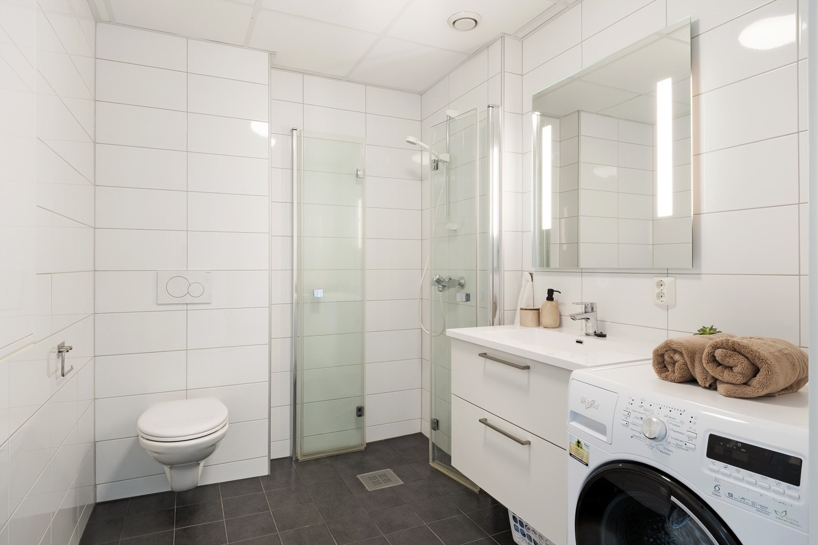 Tidlaust og romsleg heilflisa bad med varme i golvet. Badet er innreia med praktisk dusjhjørne og har opplegg for vaskemaskin. Galleribilde