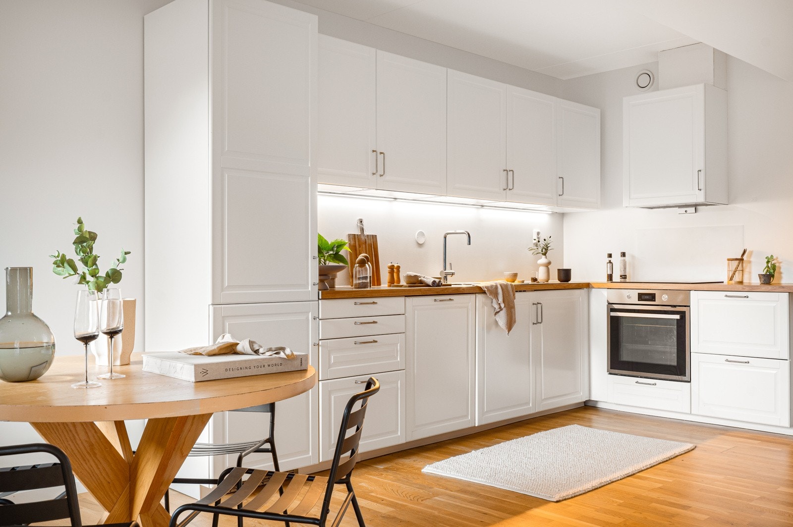 Kjøkken i L-form, med lyse profilerte fronter, integrerte hvitevarer og godt med skap- og benkeplass. Galleribilde