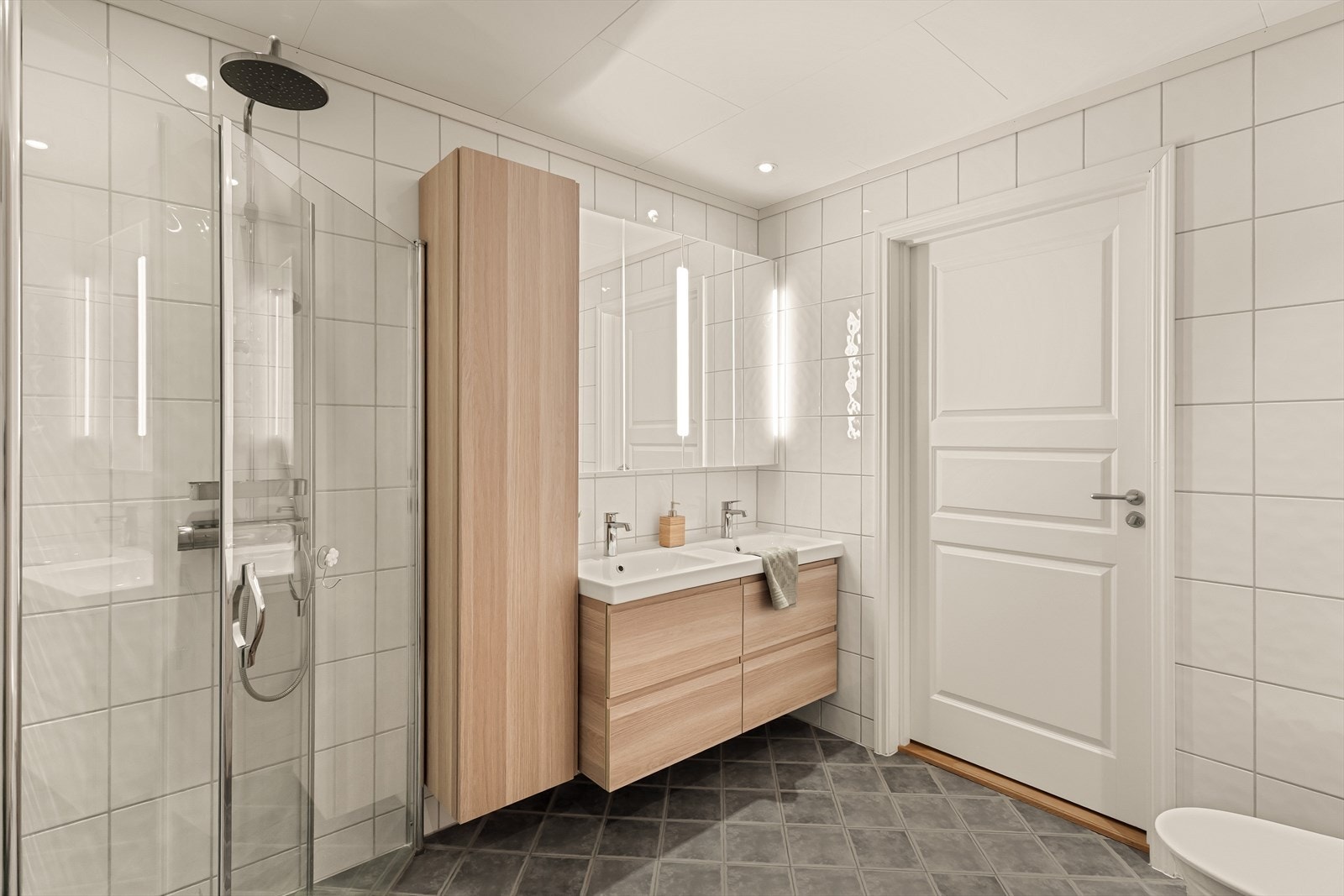 Baderomsinnredningen (fra 2020) har god oppbevaring og inneholder dobbel servant, toalett, dusjhjørne med glassdører og høyskap for praktisk lagring av håndklær og baderomsartikler. Galleribilde