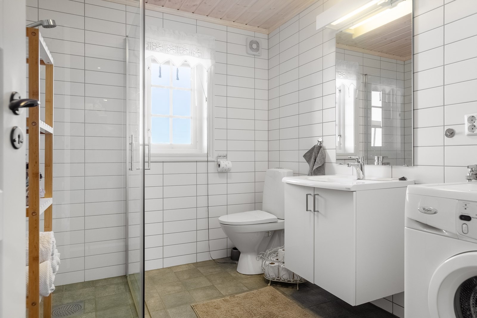 Badet er lyst og innbydende, innredet med toalett, servant, dusj og opplegg til vaskemaskin. Baderomsinnredningen er i folierte plater med servantskap, samt speil med tilhørende belysning. Galleribilde