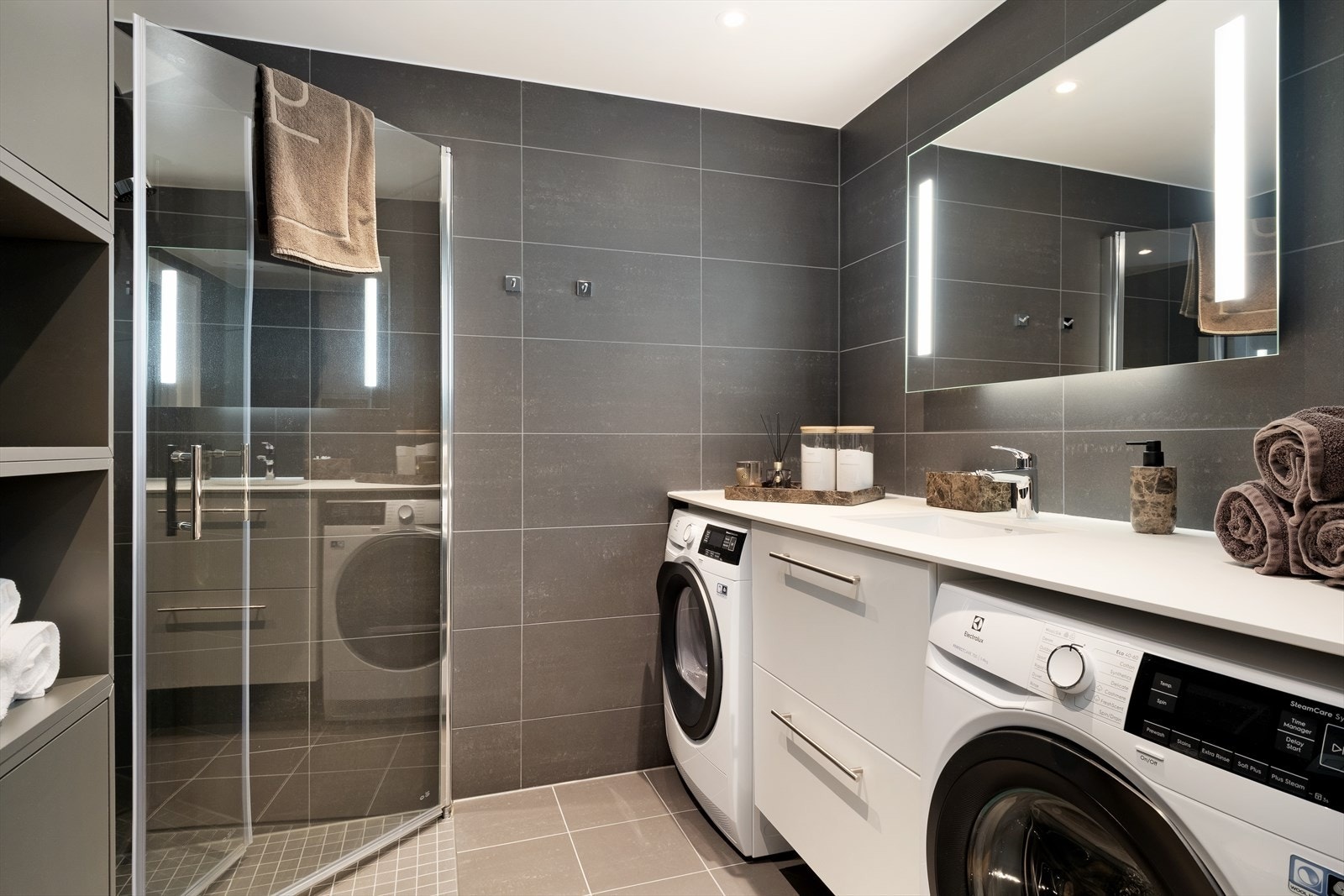 Lekkert heilflisa bad med varmekablar i golv. Badet er praktisk og smakfullt utforma, med toalett, dusjhjørne, opplegg for vaskemaskin, spegl med lys og servantmøbel. Det er montert spotlys i taket for god belysning. Galleribilde