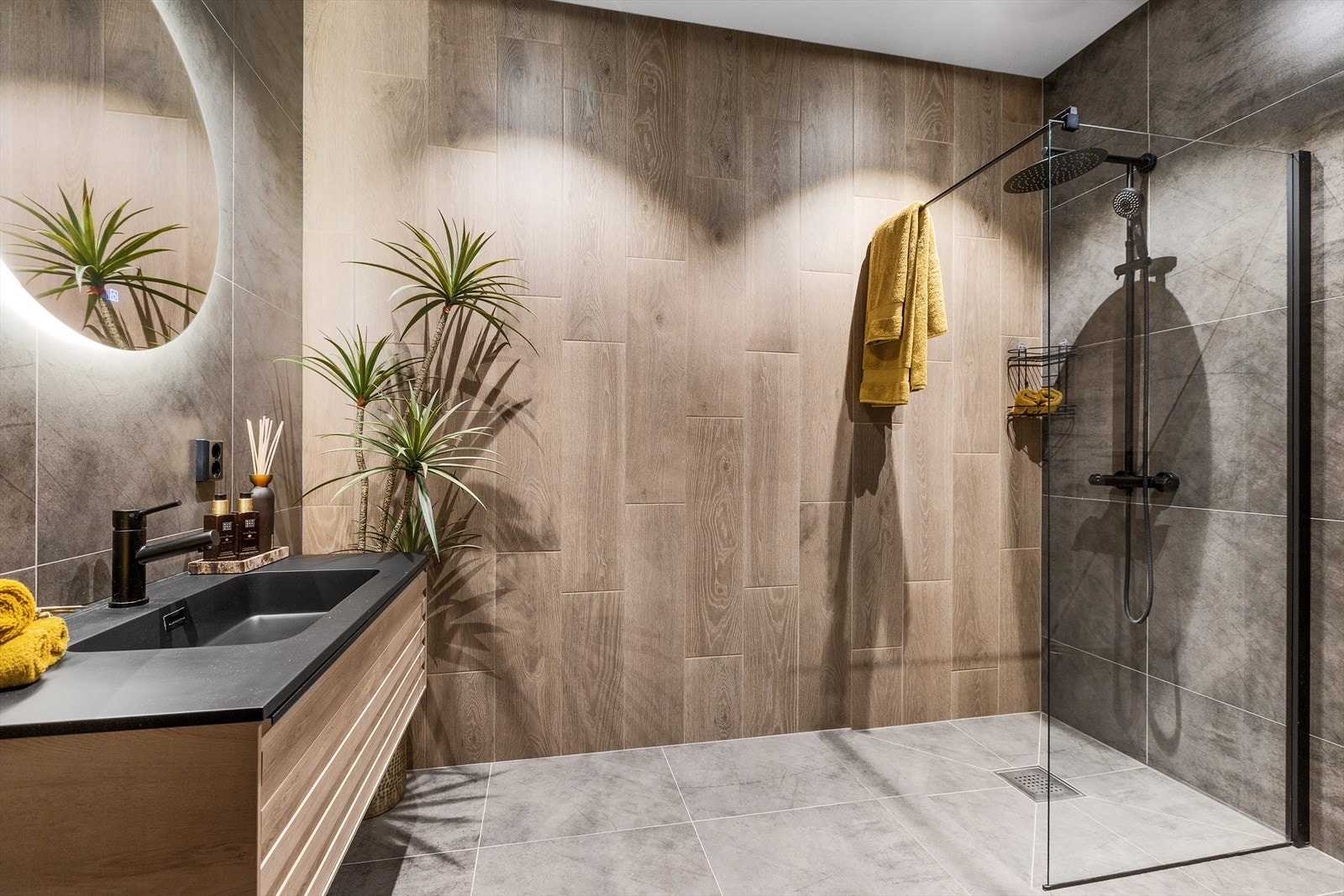 Bad/wc med Lind unique baderomsmøbel med moderne spiler i front og med rundt baderomsspeil med belysning. Vegghengt toalett, dusjhjørne med dusjvegger på 90 x 90, blandebatteri og dusjutstyr i sort utførelse Galleribilde