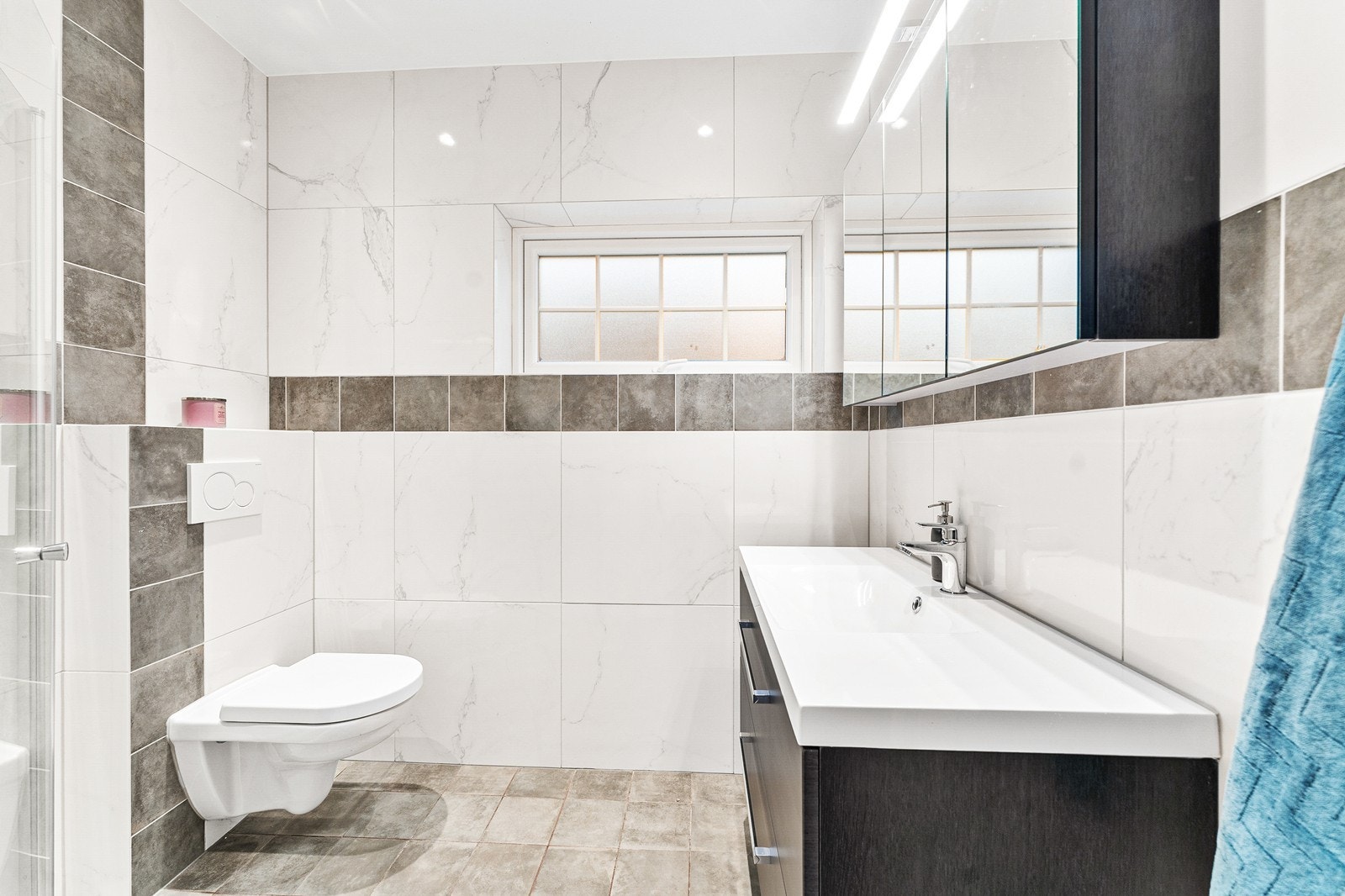 Like ved entréen finner du badet, som er utstyrt med vegghengt toalett samt dusjsone med garnityr og glassvegg. Galleribilde