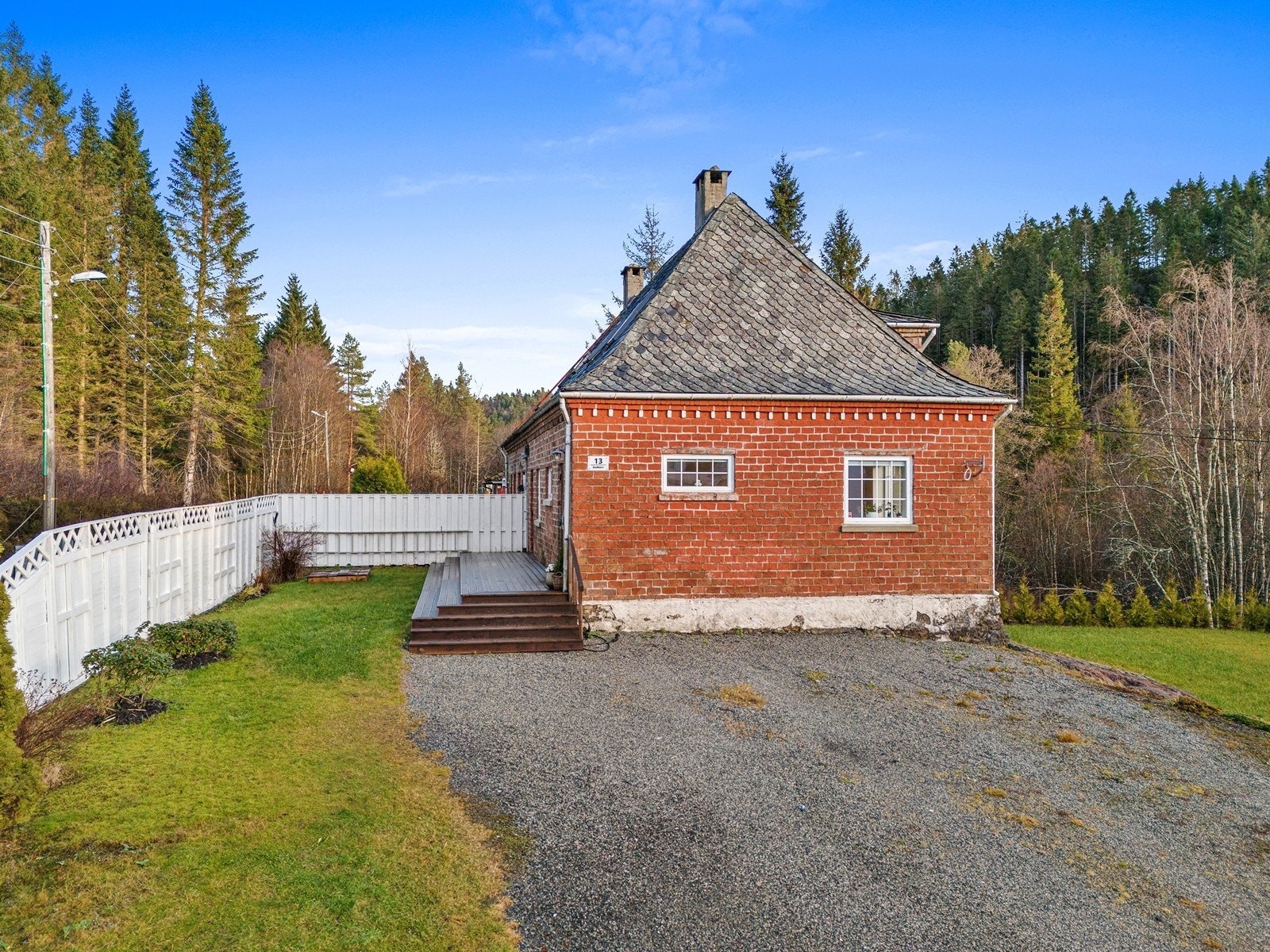 Tomten er opparbeidet med gruset parkeringsplass, plen, prydbusker og skjermvegg. Galleribilde