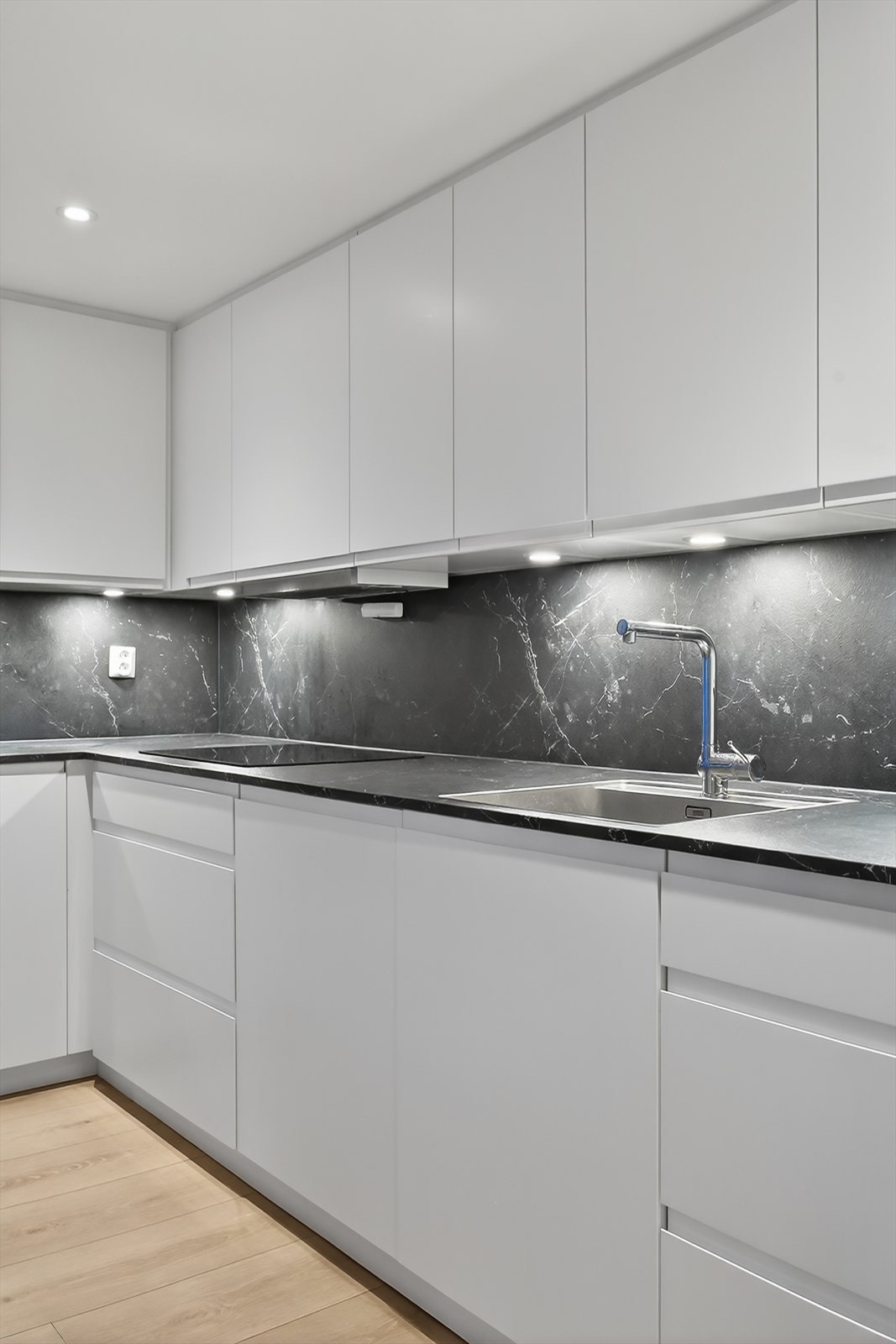 Stilrent kjøkken med glatte fronter, laminert benkeplate samt plate/spotter over benk. Galleribilde