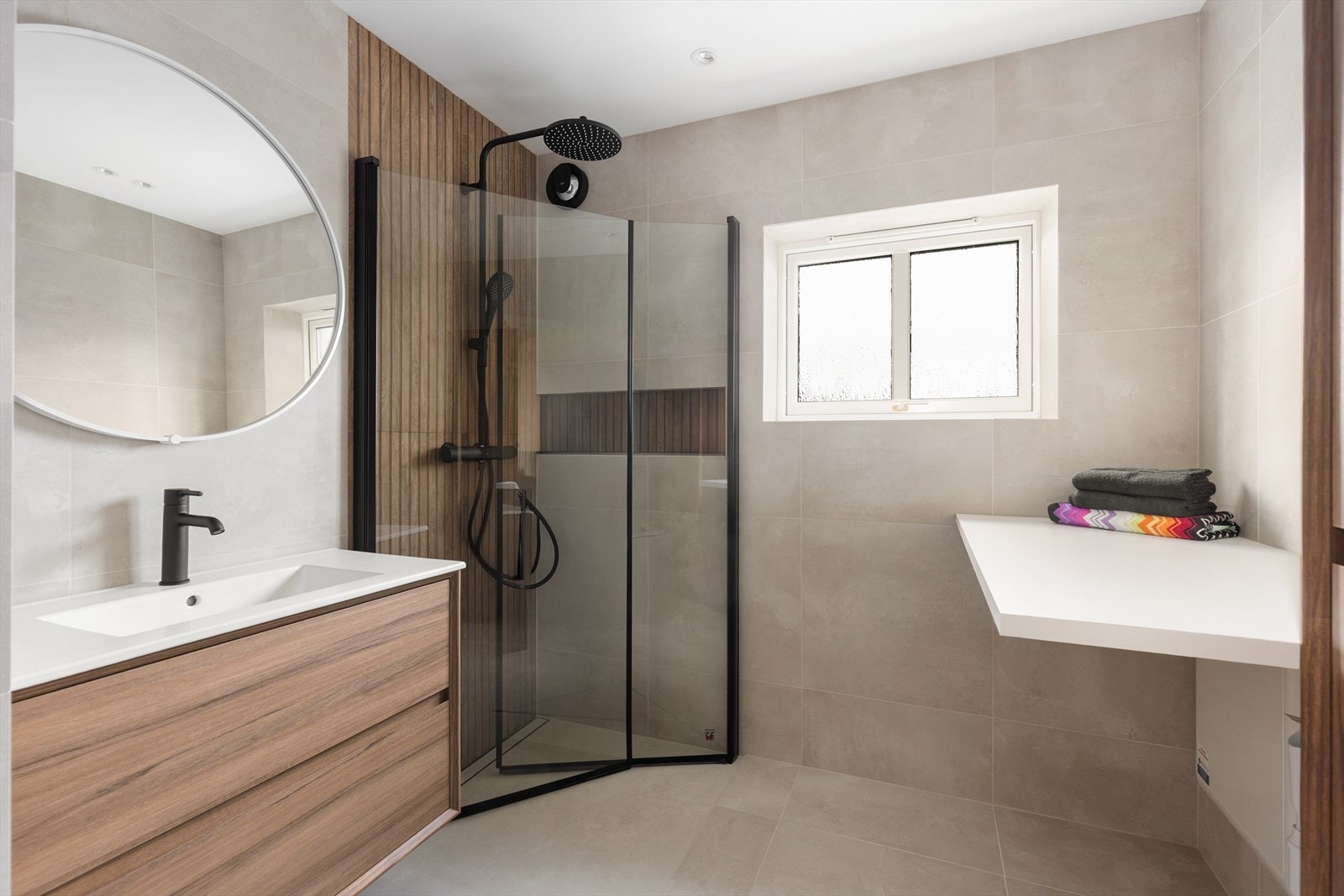 Lekkert bad fra 2025 med flis på gulv og vegger. Her er det vegghengt toalett, dusjvegger/hjørne og innredning med heldekkende hvit vask, underskuffer med slette fronter og speil. Det er i tillegg høyskap med ekstra oppbevaringsplass. Galleribilde