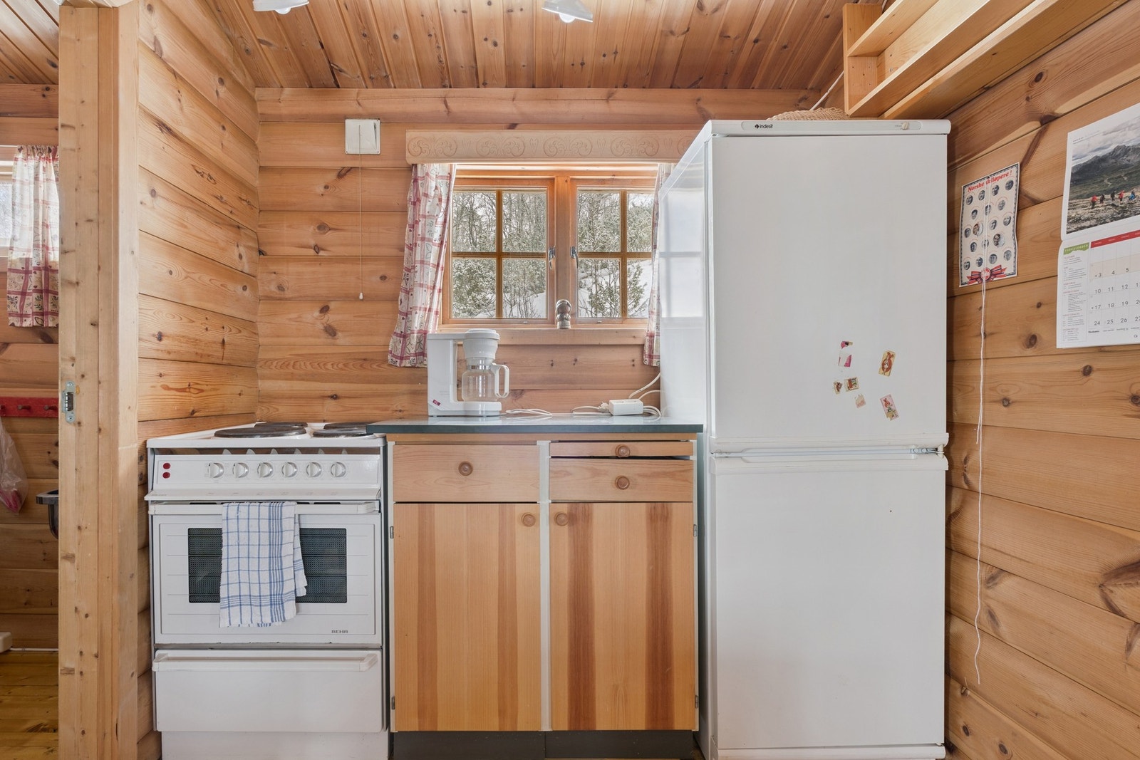 Kjøkken med enkel innredning og frittstående komfyr og kombi-kjøleskap. Galleribilde