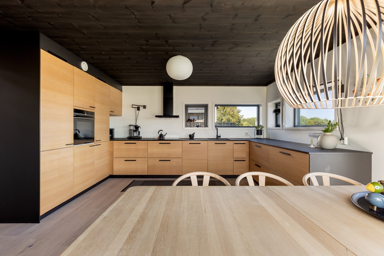 Hel seksjon med høyskap på den ene veggen med integrert kjøl/fryseskap og stekeovn i praktisk arbeidshøyde. Gode arbeidsflater på laminert benkeplate med godt arbeidslys fra vinduer over benk. Galleribilde