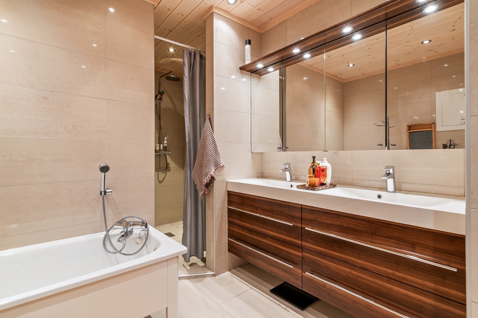 Rommet er innredet med badekar og dusjnisje med mosaikkfliser, vegghengt toalett og stor servantseksjon med skuffer som gir ekstra oppbevaringsplass. Galleribilde