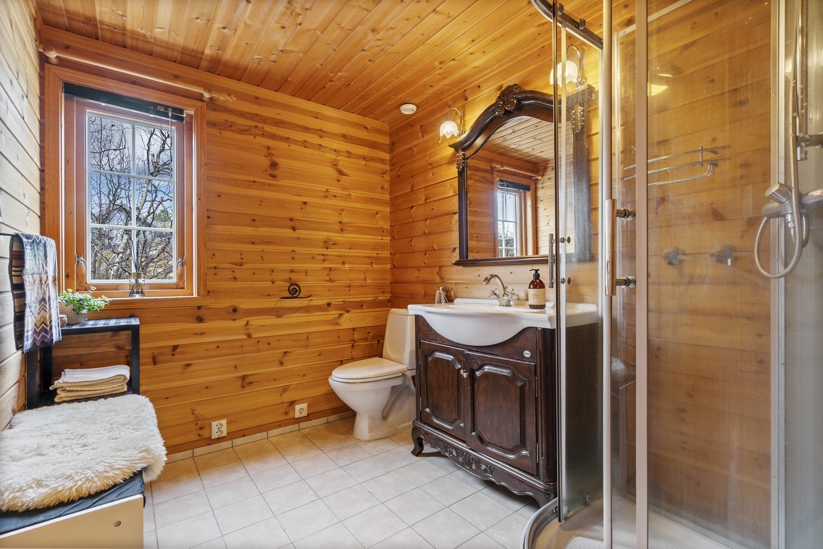 Badet er utstyrt med gulvmontert toalett, servant med innredning og dusjkabinett. Gulvet er flislagt og har varmekabler som gir ekstra komfort. Galleribilde