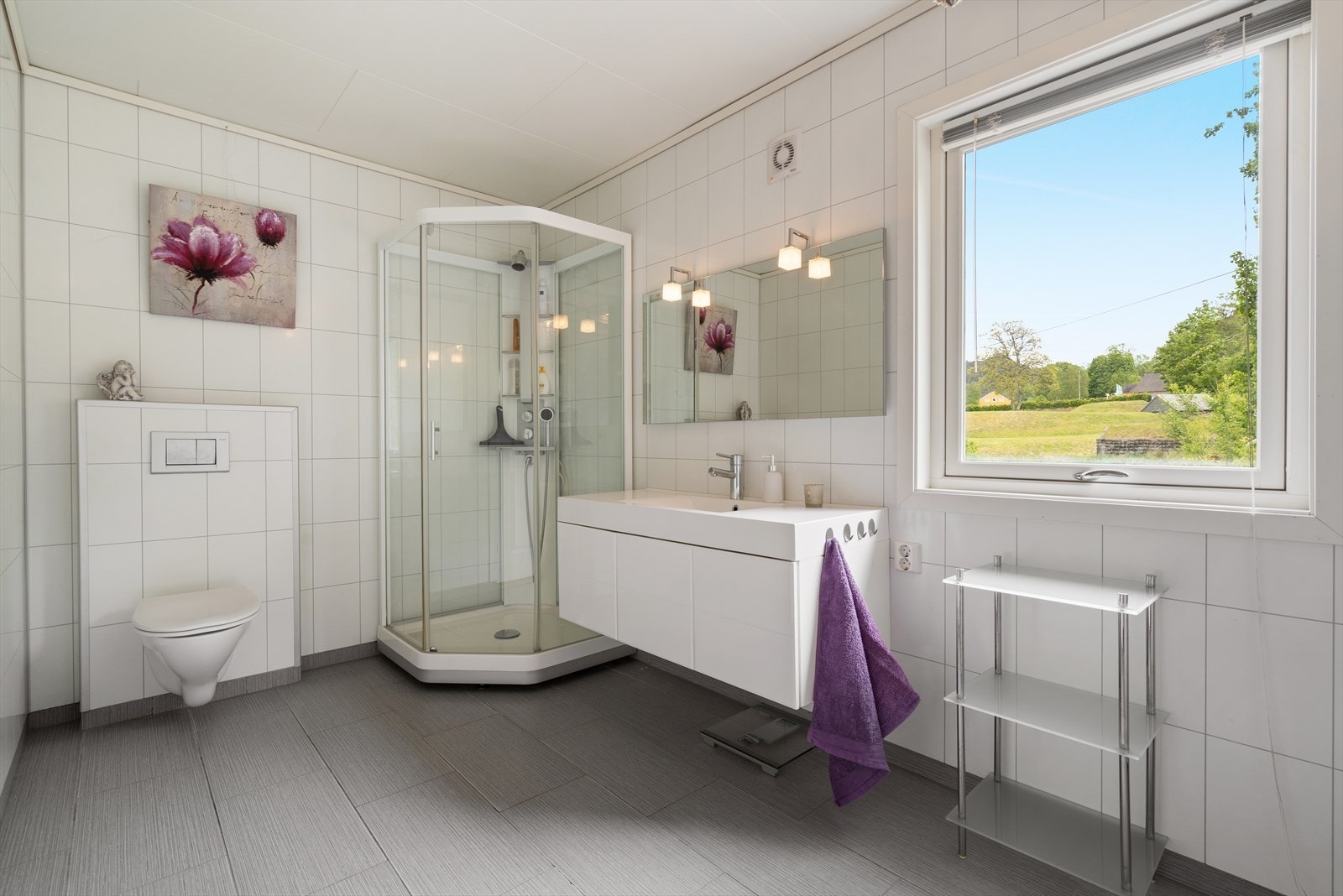 Badet i første etasje har fliser på gulv og baderomsplater på veggene, og er innredet med vegghengt toalett, servant med innredning og dusjkabinett. Galleribilde