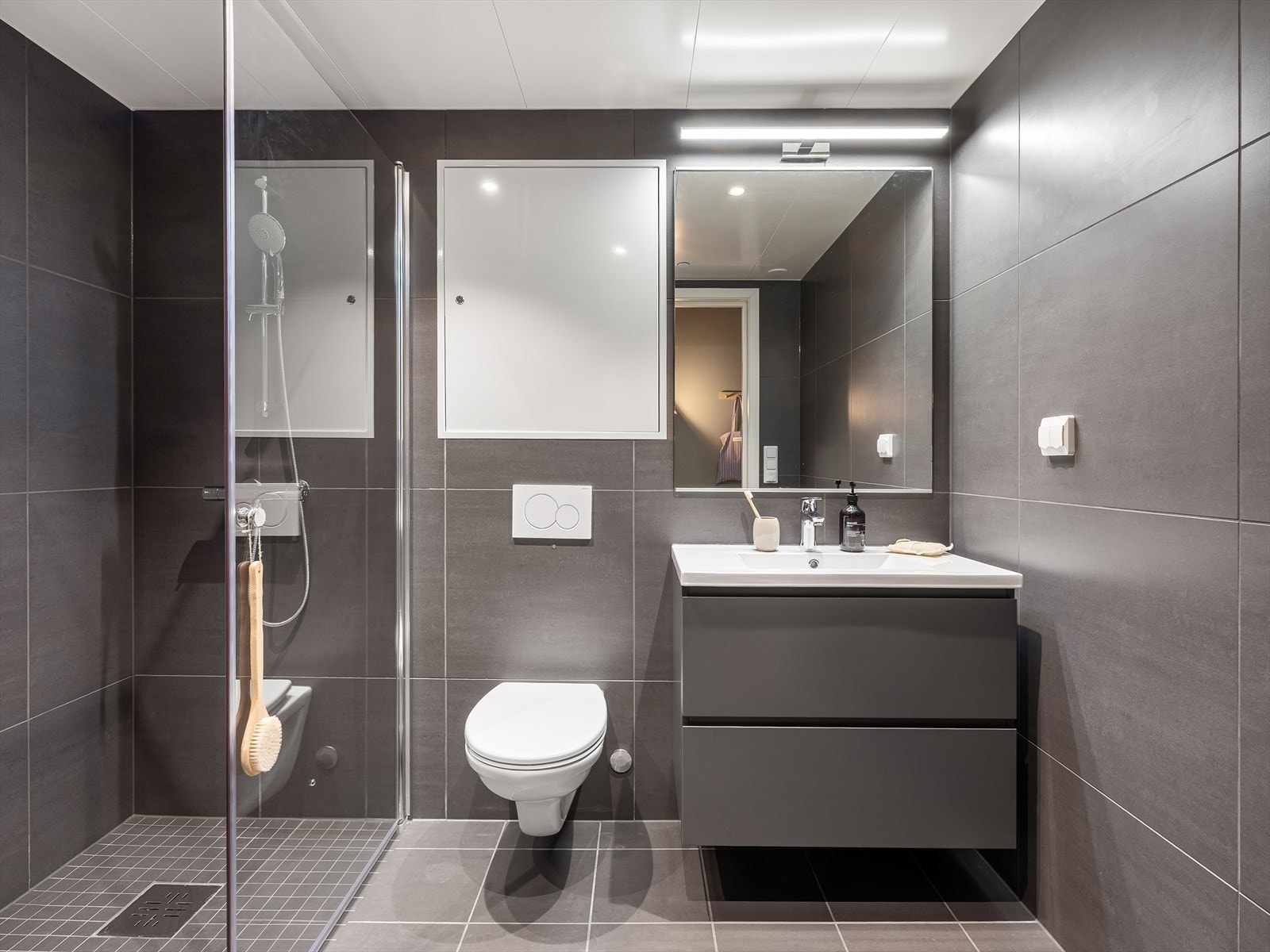 Badet er innredet med servant med underskuffer, speil med overlys, veggmontert WC og et romslig dusjhjørne. Galleribilde