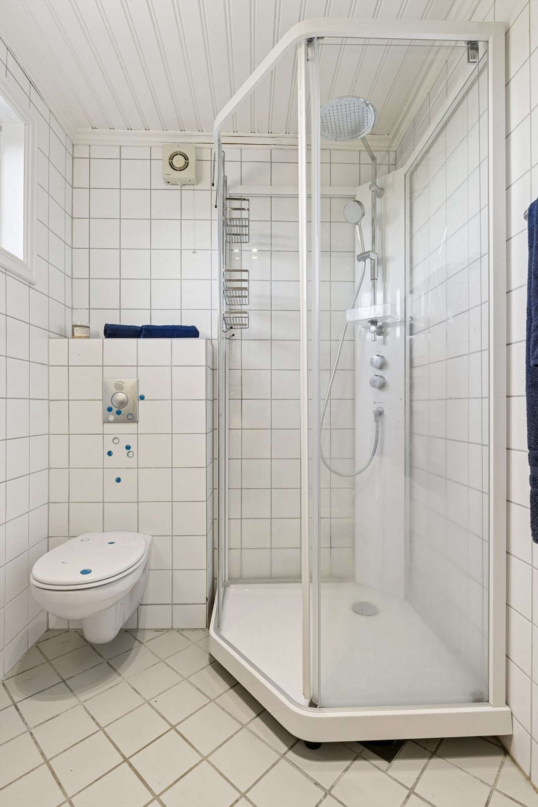 Flislagt baderom av eldre dato. Badet er innredet med veggmontert wc, servantinnredning og dusjkabinett. Galleribilde