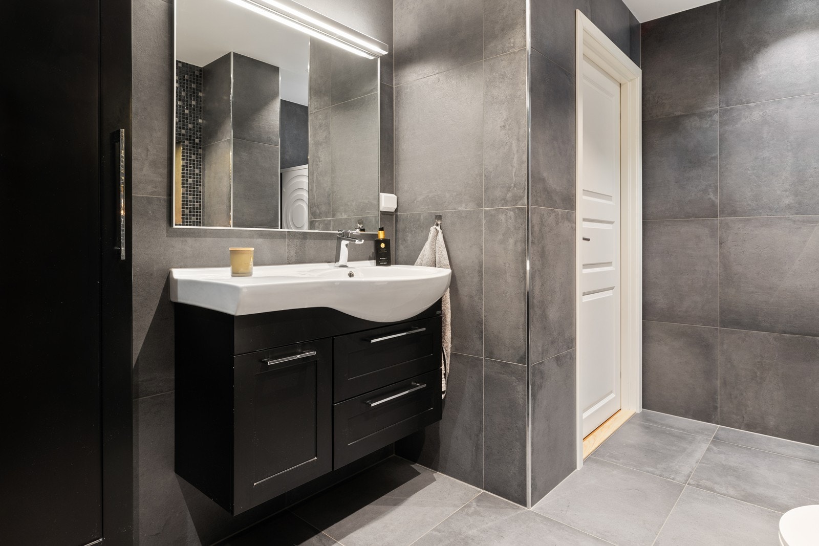 Badet har moderne innredning med skuffer og skap, speil med lys Galleribilde