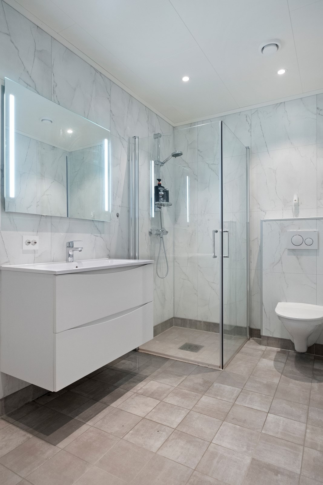 Dusjhjørne med glassdører og vegghengt toalett gir en effektiv utnyttelse av rommet. Galleribilde